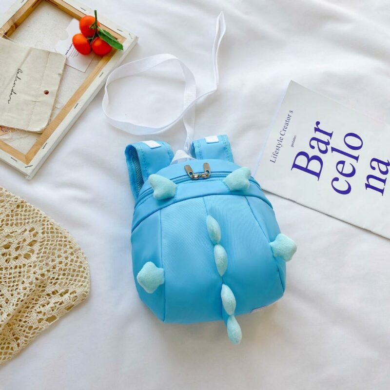 Zaino prescolare a forma di dinosauro blu con sfondo letto bianco e poster bianco con scritte blu