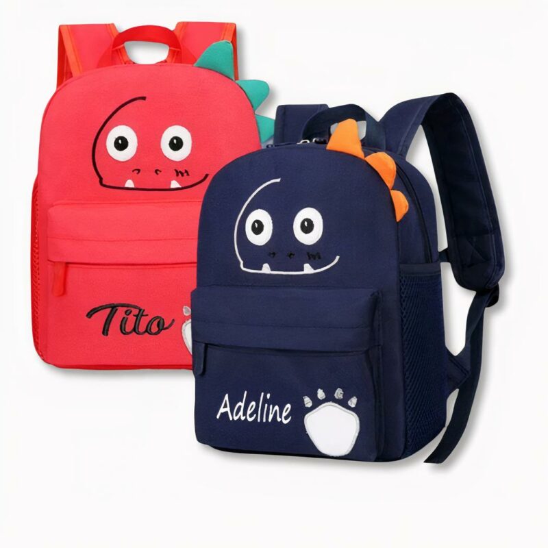 2 zaini per bambini, uno rosso e uno blu scuro, con volti di dinosauri sorridenti personalizzati con i nomi di Tito e Adeline, su sfondo grigio chiaro