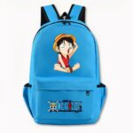 Foto di uno zaino di One Piece di colore azzurro. Lo zaino presenta un disegno sul davanti della versione manga del personaggio Luffy, che è seduto con una maglietta rossa, tiene il cappello nella mano sinistra e spalanca la bocca. La tasca anteriore presenta il logo di One Piece con un motivo di teschio e ossa incrociate e una scritta blu. La borsa è dotata anche di tasche laterali. Lo sfondo dell'immagine è grigio chiaro.