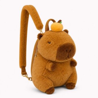 Un sac à dos capybara assis tenant un fruit rond en peluche marron, avec bretelle rembourrée et petite pomme sur la tête, posé sur fond blanc.